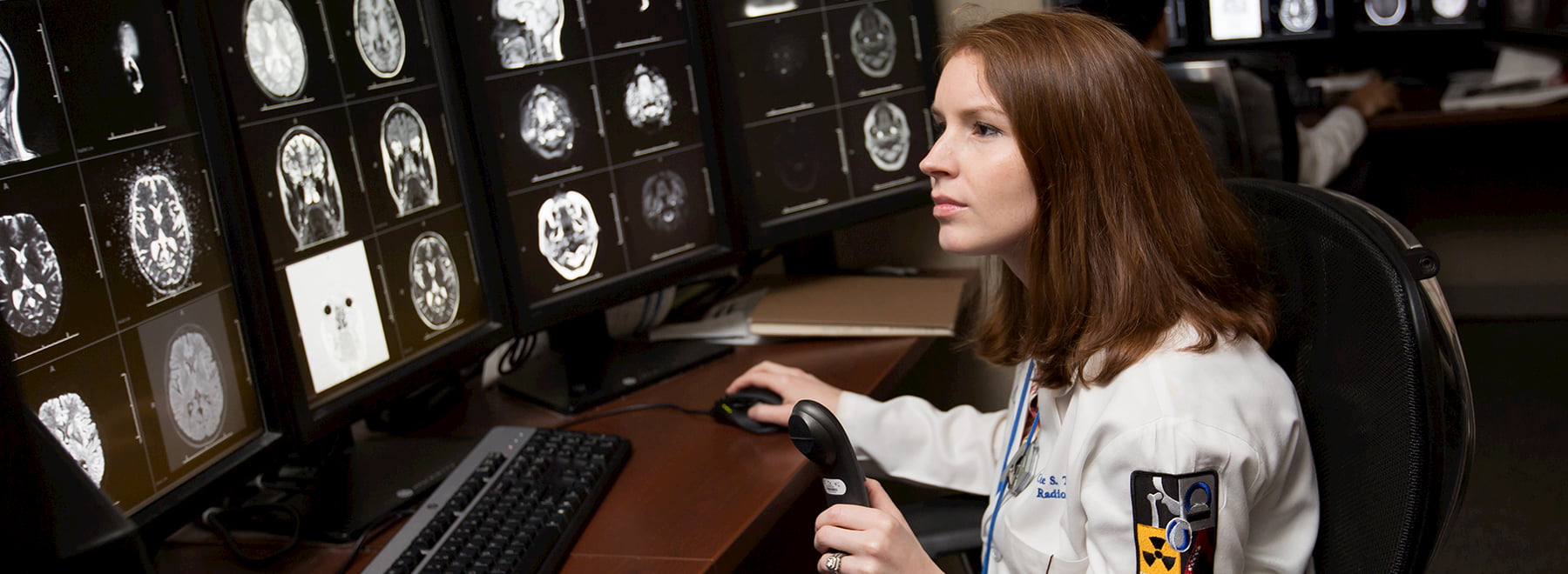 Seated female radiologist reviews images of the human brain on several computer screens.